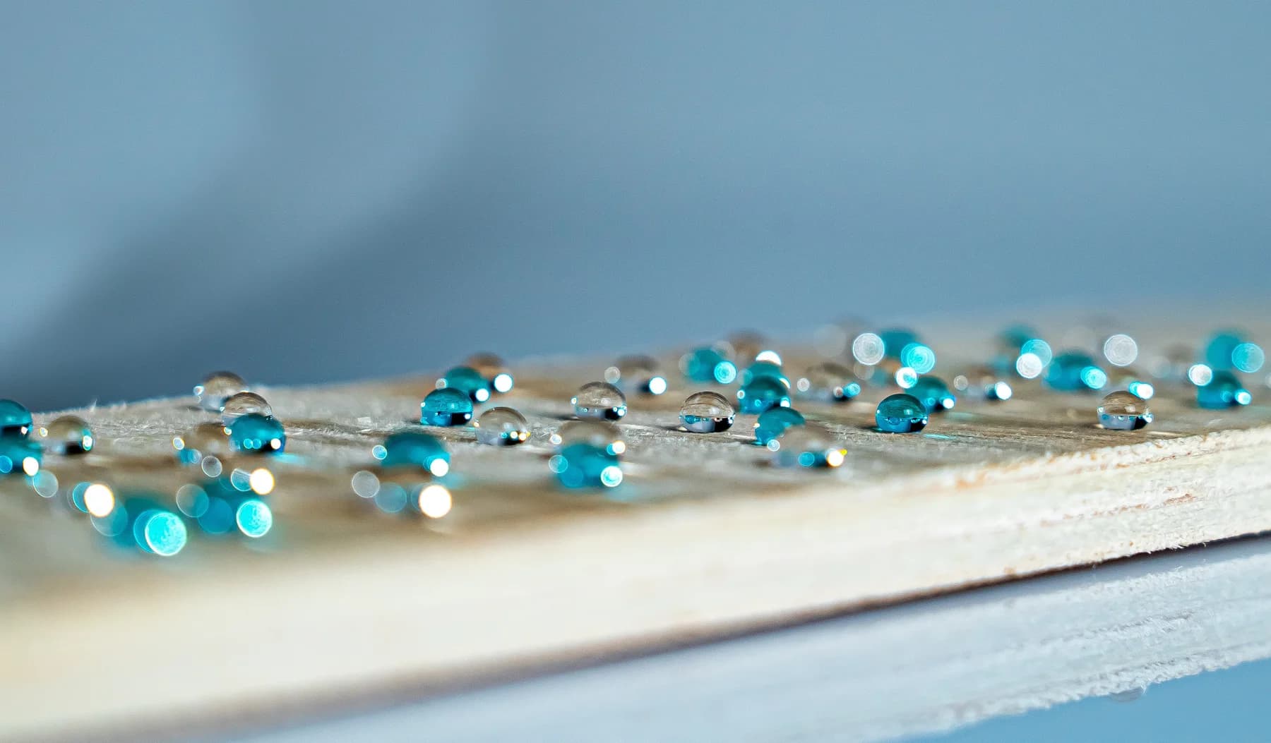 Clear and blue water droplets beading on a natural wood sample